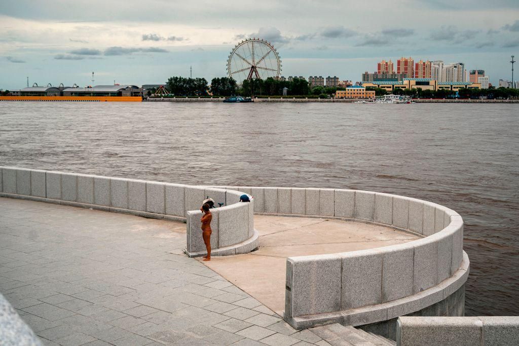 Uma mulher está em uma margem do rio Amur, com a cidade chinesa de Heihe vista ao fundo, na cidade russa de Blagoveshchensk, no extremo leste, em 17 de agosto de 2020. (Foto de Dimitar DILKOFF / AFP) (Foto de DIMITAR DILKOFF / AFP via Getty Images)